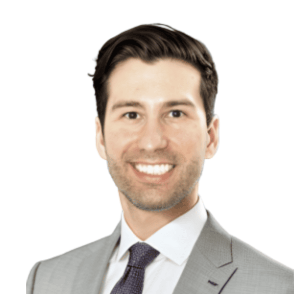 Smiling man with short dark hair wearing a grey suit jacket, white shirt, and dark tie, posed against a plain white background.