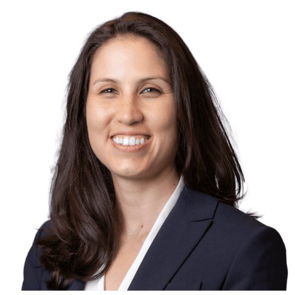 Woman with long brown hair wearing a navy blazer and white blouse, smiling at the camera against a white background.