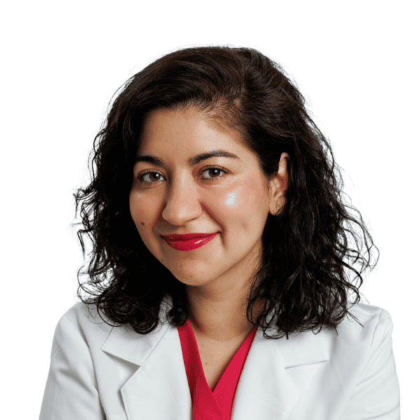 A woman with curly dark hair, wearing a white lab coat and a red top, smiles at the camera against a plain white background.