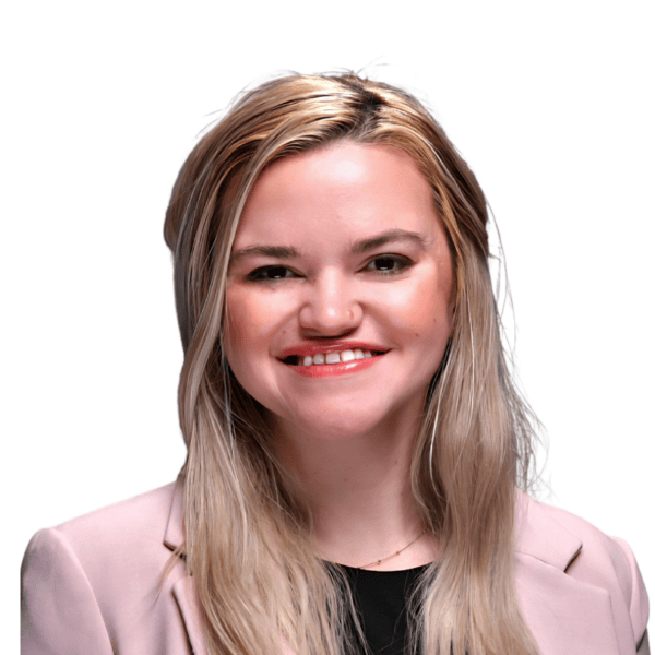Smiling woman with long blonde hair, wearing a light pink blazer over a black top, posed against a plain white background.